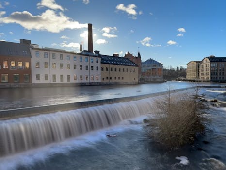 Scenic view of a cascading waterfall alongside historical city architecture under a bright sky.